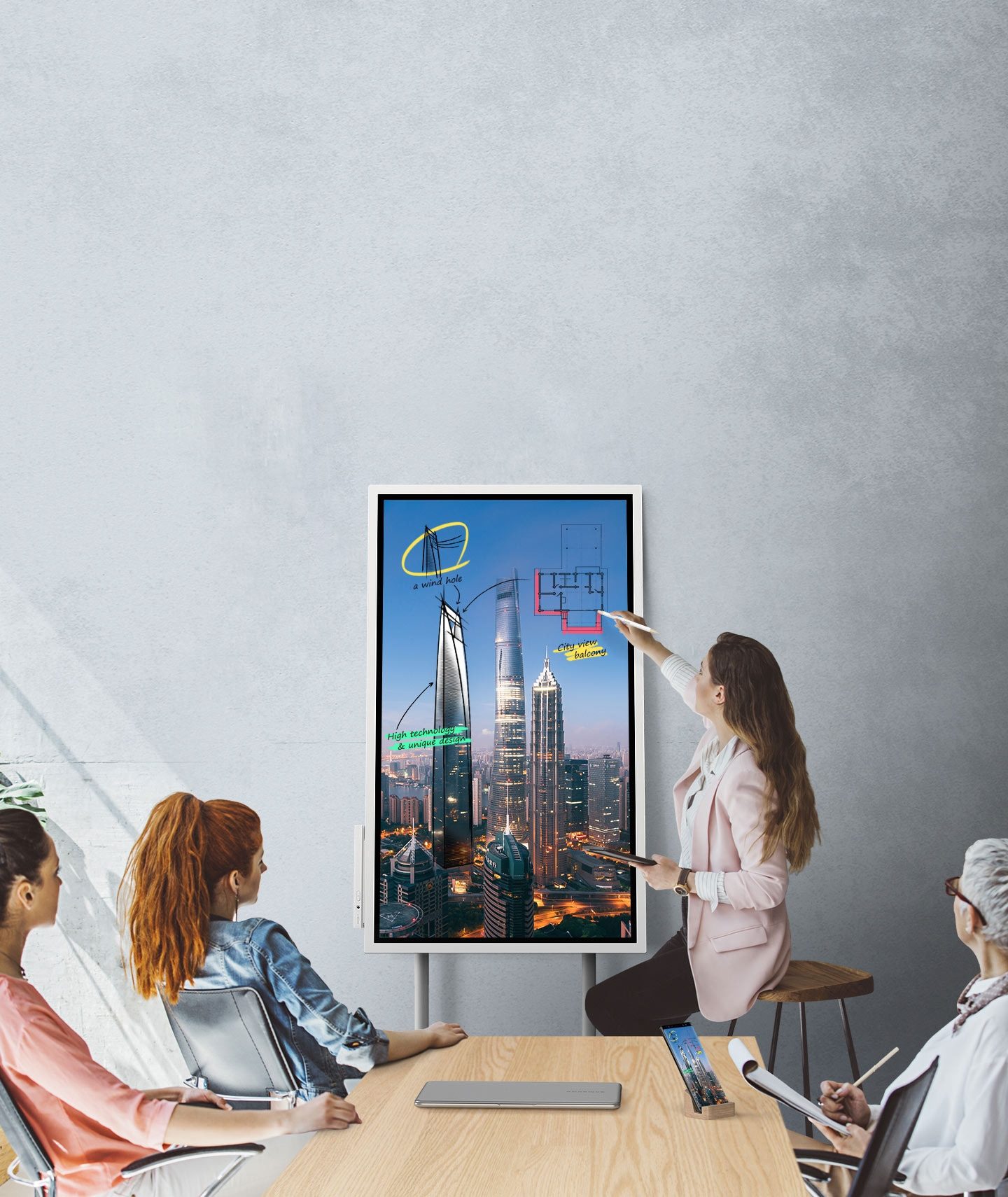 Una imagen que muestra a cuatro personas en una reunión donde se conectan un dispositivo Samsung Flip y un teléfono inteligente, mostrando las mismas imágenes. Miran la pantalla del Samsung Flip posicionado en modo Portait y dos de ellos toman notas.