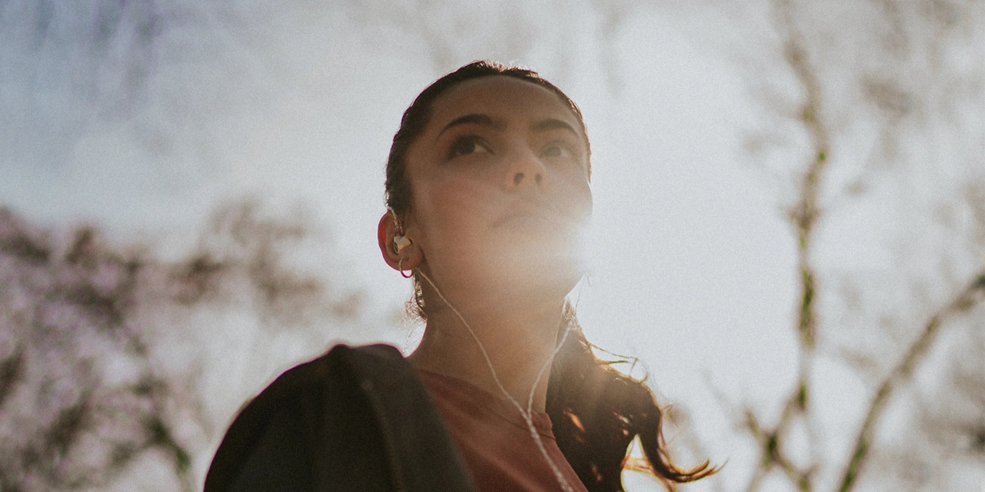 Mujer joven con los mejores auriculares con cable Meze Audio Alba, vista desde abajo con el sol al fondo